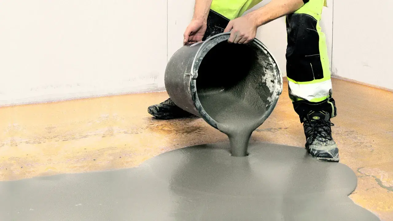 Person i varselkläder häller flytspackel på ett garagegolv för att jämna ut det.