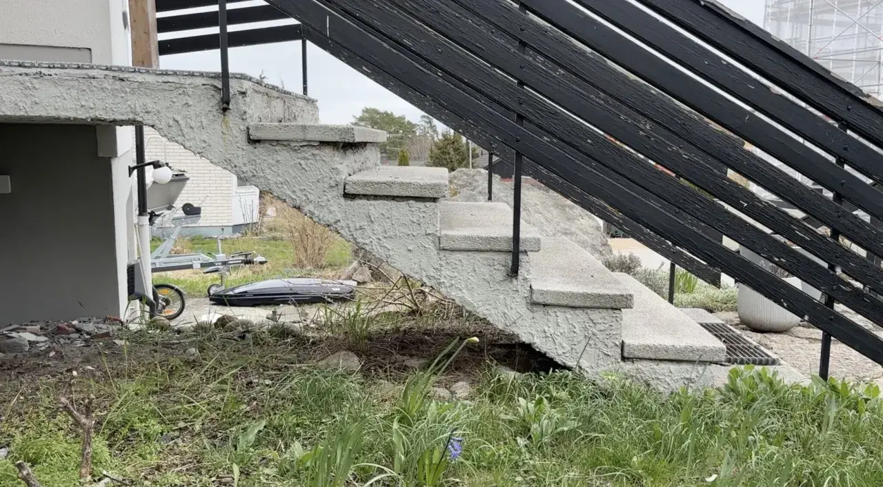 Grå betongtrappa med svarta räcken. En trailer och takbox syns i bakgrunden. Undrar du över gjuta trappa kostnad?