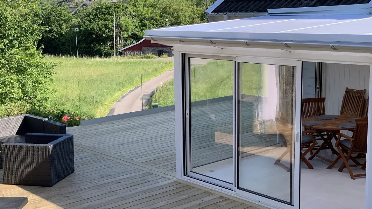 Nybyggd altan med glaspartier och utemöbler. En vacker utsikt över grönskande landskap. Bra att veta om bygga trall kostnad.