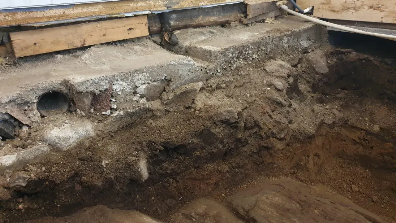 Grundläggning för att bygga på berg. Synliga stenar, jord och delar av en gammal betonggrund.