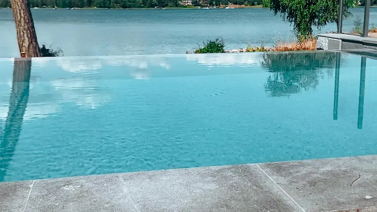 En vacker infinity pool som speglar himlen och omgivande träd. Drömmen om att bygga infinity pool vid en sjö.