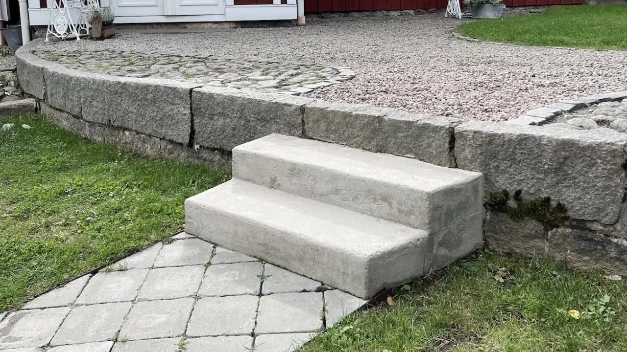 Nya gjuta trappsteg i betong leder upp från en stenlagd gång.