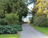 Vacker trädgård med en blåvit villa i bakgrunden. En grusväg leder fram till huset, kantad av frodiga växter och träd. Man ser hur man kan plantera buskar i grupp för att skapa en lummig miljö.