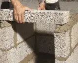 Händer lägger lecablock direkt på marken, bygger en mur med cement.