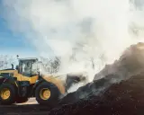 Gul hjullastare arbetar med en stor hög av organiskt material, ånga stiger. En bra indikation på schakt pris per kubik.
