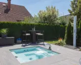 En liten tomt med en pool och ett utomhusdusch. En sittgrupp med bord och stolar står vid en häck.
