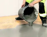 Person i varselkläder häller flytspackel på ett garagegolv för att jämna ut det.