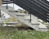 Grå betongtrappa med svarta räcken. En trailer och takbox syns i bakgrunden. Undrar du över gjuta trappa kostnad?