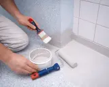 Måla plastmatta badrum med pensel och roller. En hink med färg står bredvid.