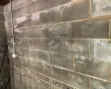 Grå lecablockvägg med fuktfläckar och en rördragning. Förberedelser för att putsa lecablock under mark.