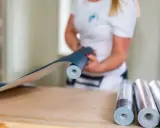 En person håller i en rulle mörkblå tapet, redo att måla på tapet. Fler rullar ligger på bordet.