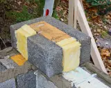 Isolering av lecablock med glasull. En bit trä ligger mellan blocken.