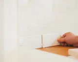 En hand placerar en vit kakelplatta mot en vägg med fix. Det är ett noggrant arbete att kakla på kakel.