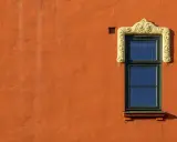 Ett fönster med en utsmyckad, gul ram på en orange, putsad fasad. Man undrar om det är här man måste måla putsad fasad för att bevara dess charm.