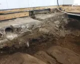 Grundläggning för att bygga på berg. Synliga stenar, jord och delar av en gammal betonggrund.