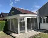 Ett modernt uterum med glaspartier och en vit takkonstruktion. Taklutningen på det angränsande huset ger en fin kontrast.
