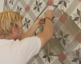 Man foga om kakel med en spackel. Mönstret på kaklet är geometriskt med stjärnor i grått, vitt och rött.