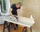 Man spacklar plywood med en cirkelsåg på en skena.