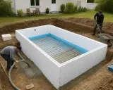 Byggnation av en pool med betongstomme. En person pumpar betong medan en annan fyller skottkärra.