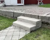 Nya gjuta trappsteg i betong leder upp från en stenlagd gång.