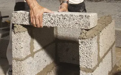 Händer lägger lecablock direkt på marken, bygger en mur med cement.