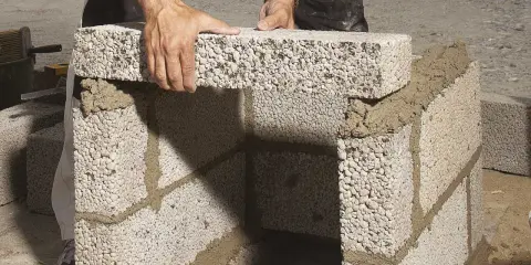 Händer lägger lecablock direkt på marken, bygger en mur med cement.