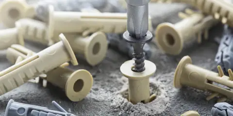 En skruv dras in i en plugg omgiven av olika skruvar och pluggar i grått och beige.