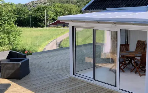 Nybyggd altan med glaspartier och utemöbler. En vacker utsikt över grönskande landskap. Bra att veta om bygga trall kostnad.