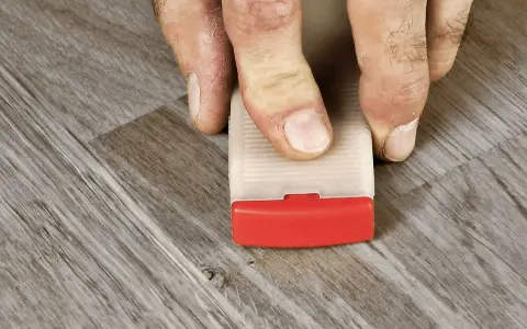 Fingrar trycker ner en kil för att laga laminatgolv.