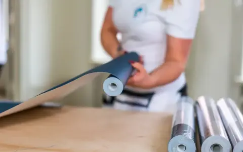 En person håller i en rulle mörkblå tapet, redo att måla på tapet. Fler rullar ligger på bordet.