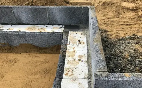 Grunden byggs med lecablock. Sand och grus ligger runt den pågående konstruktionen.