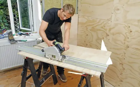 Man spacklar plywood med en cirkelsåg på en skena.