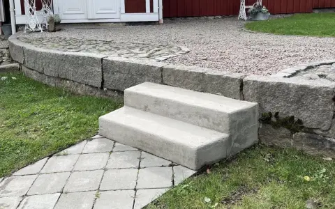 Nya gjuta trappsteg i betong leder upp från en stenlagd gång.