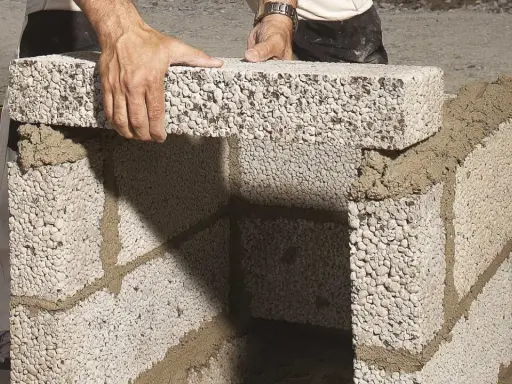 Händer lägger lecablock direkt på marken, bygger en mur med cement.