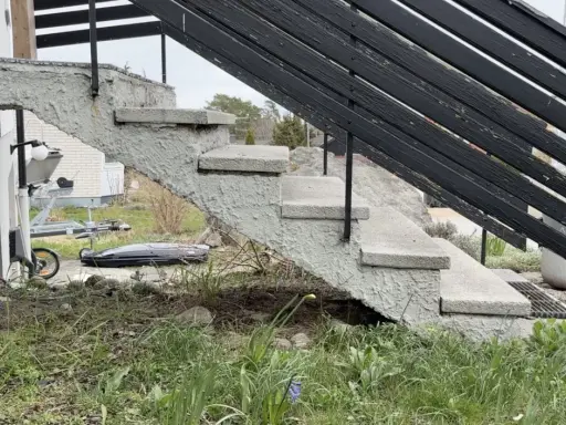 Grå betongtrappa med svarta räcken. En trailer och takbox syns i bakgrunden. Undrar du över gjuta trappa kostnad?