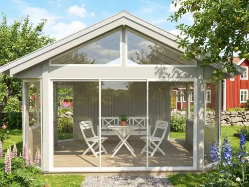 Ett fristående uterum på 25 kvm med glaspartier och skjutdörrar, möblerat med bord och stolar. Omgivet av en lummig trädgård med blommor och ett rött hus i bakgrunden.