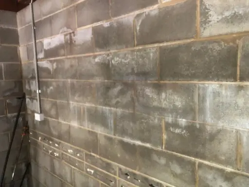 Grå lecablockvägg med fuktfläckar och en rördragning. Förberedelser för att putsa lecablock under mark.