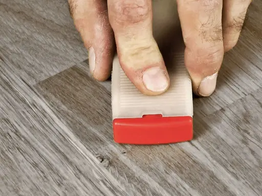 Fingrar trycker ner en kil för att laga laminatgolv.