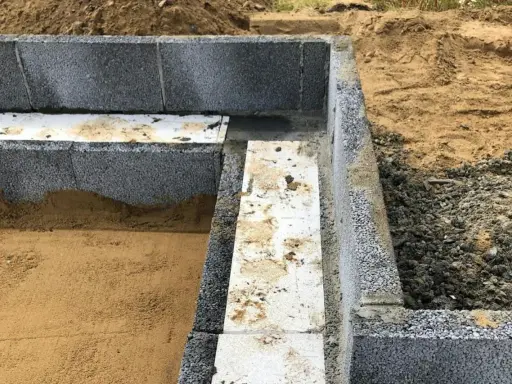 Grunden byggs med lecablock. Sand och grus ligger runt den pågående konstruktionen.