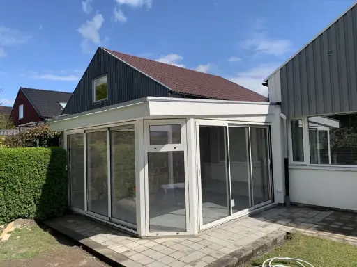 Ett modernt uterum med glaspartier och en vit takkonstruktion. Taklutningen på det angränsande huset ger en fin kontrast.