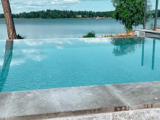 En vacker infinity pool som speglar himlen och omgivande träd. Drömmen om att bygga infinity pool vid en sjö.