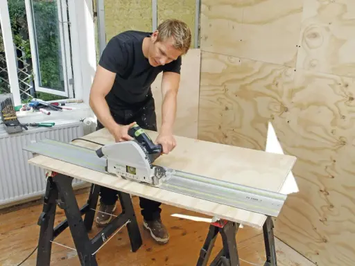 Man spacklar plywood med en cirkelsåg på en skena.