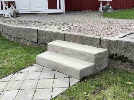 Nya gjuta trappsteg i betong leder upp från en stenlagd gång.