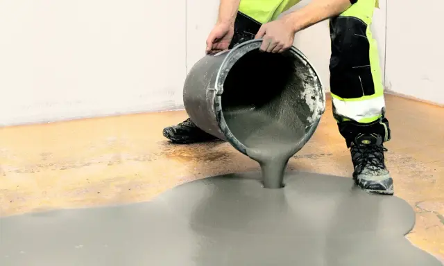 Person i varselkläder häller flytspackel på ett garagegolv för att jämna ut det.