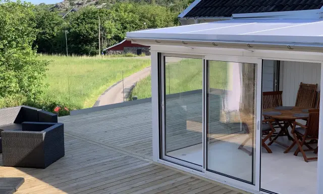 Nybyggd altan med glaspartier och utemöbler. En vacker utsikt över grönskande landskap. Bra att veta om bygga trall kostnad.