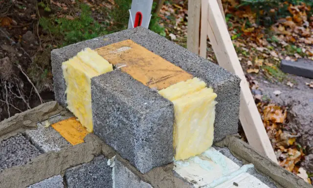 Isolering av lecablock med glasull. En bit trä ligger mellan blocken.