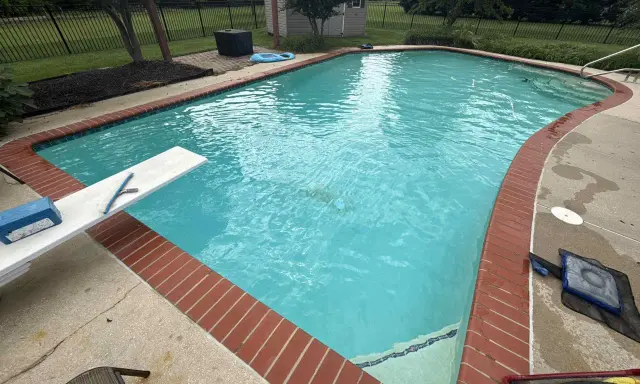 En stor pool med turkost vatten, en vit dykbräda med rengöringsredskap och en liten blå uppblåsbar leksak. Man kan undra hur mycket vatten rymmer en pool av denna storlek.