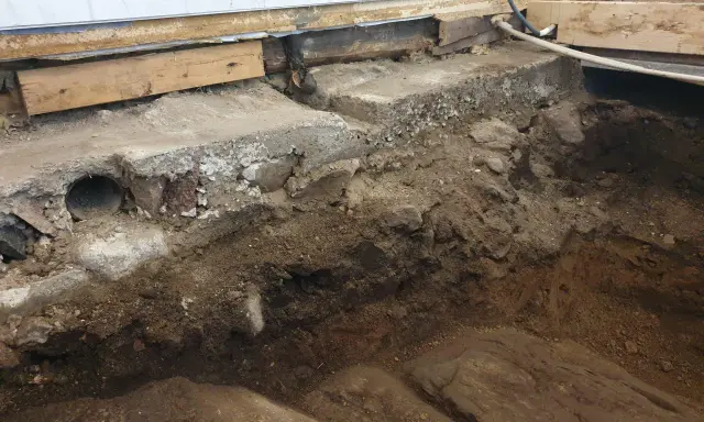 Grundläggning för att bygga på berg. Synliga stenar, jord och delar av en gammal betonggrund.