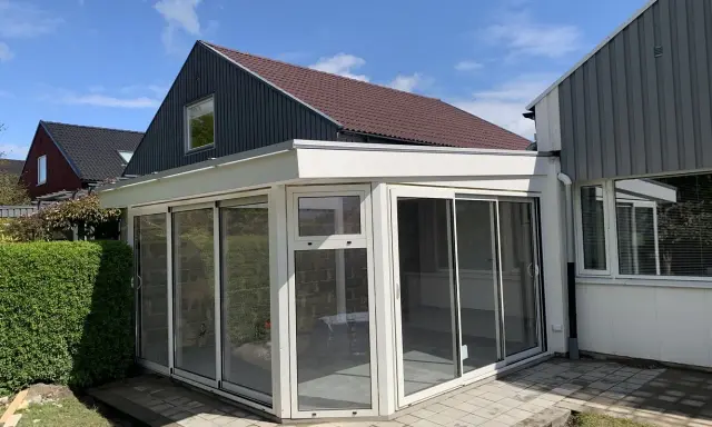 Ett modernt uterum med glaspartier och en vit takkonstruktion. Taklutningen på det angränsande huset ger en fin kontrast.