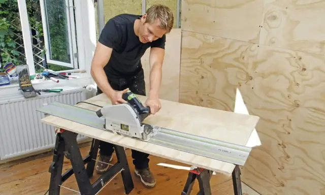 Man spacklar plywood med en cirkelsåg på en skena.